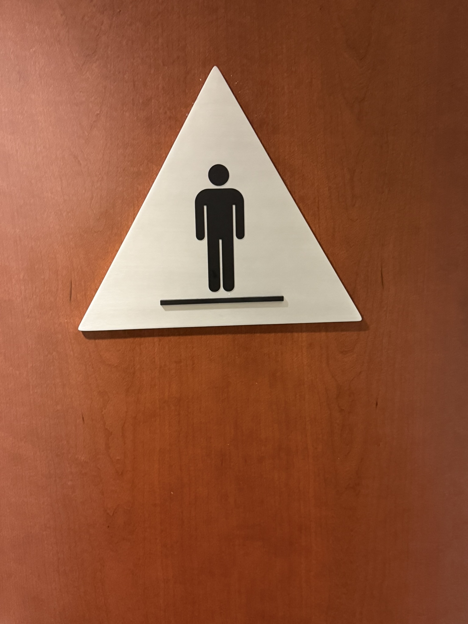 Triangular restroom identification sign with a male pictogram mounted on a wood door