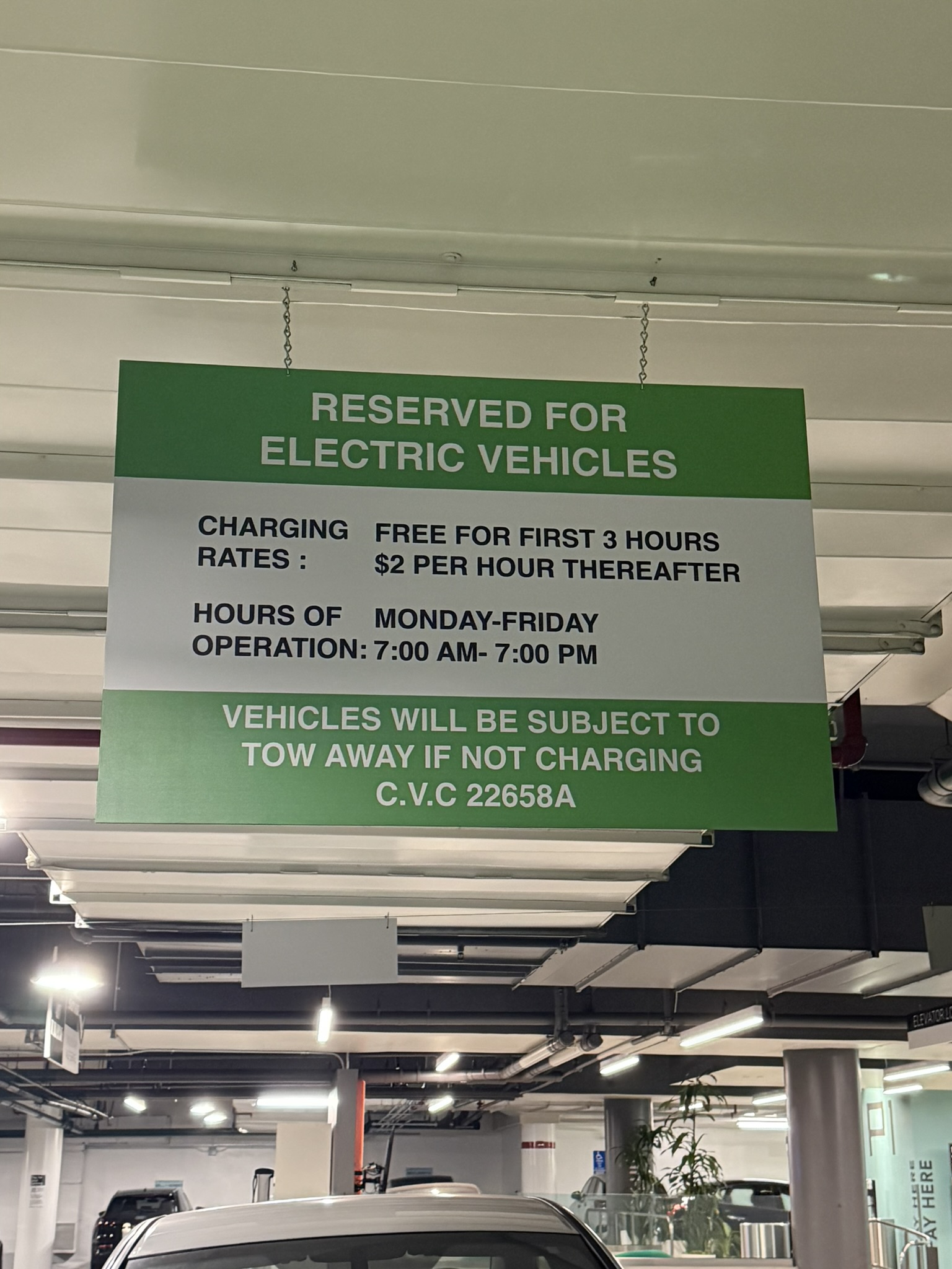 Green and white hanging sign reserving parking for electric vehicles, with charging rates and operating information