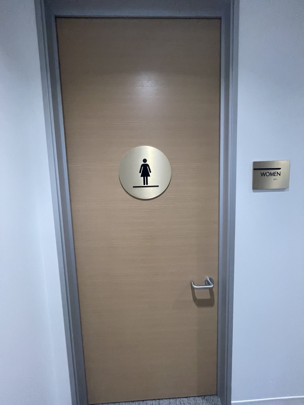 Circular women’s restroom pictogram on a wood door beside a matching Women wall sign