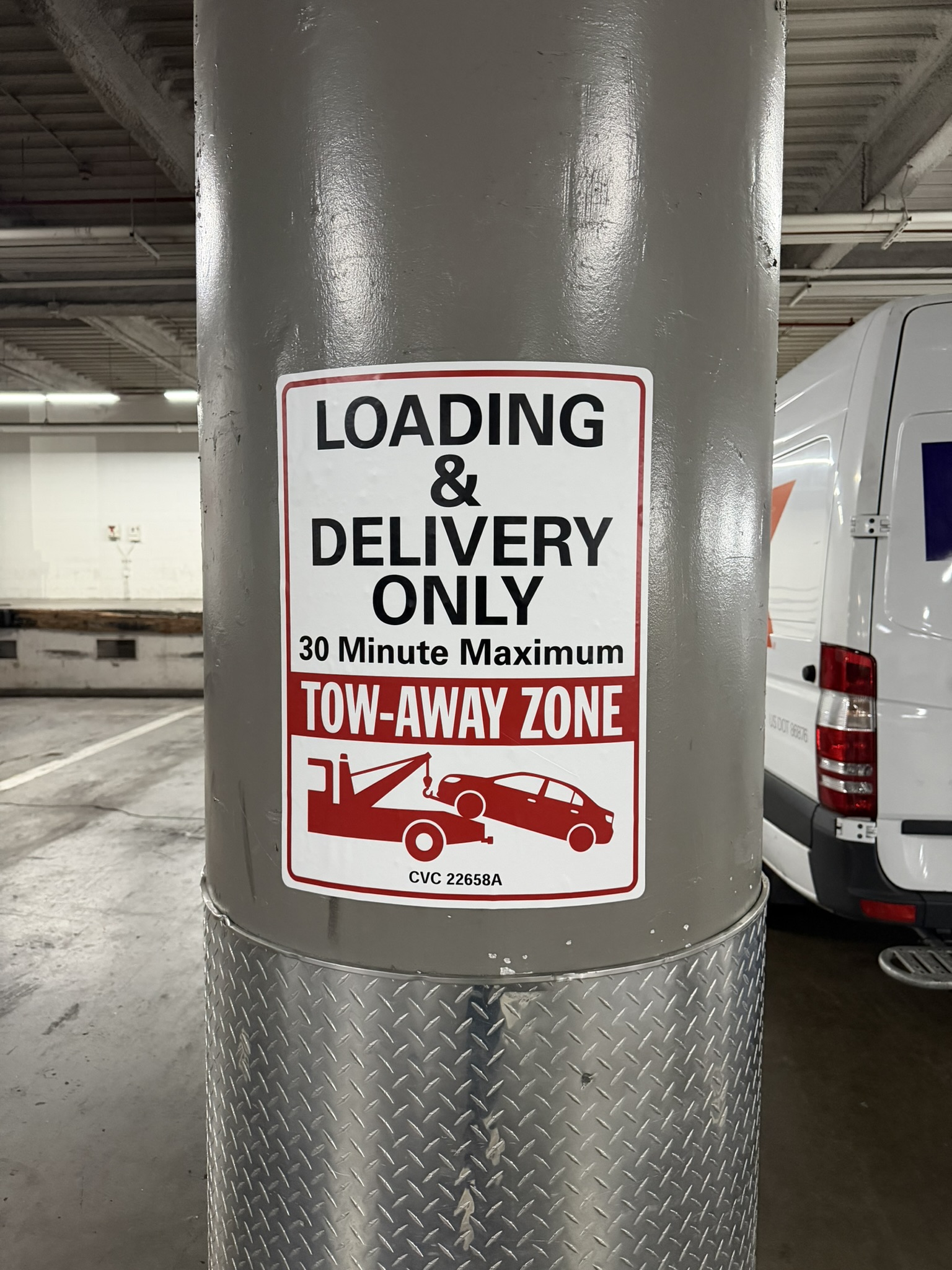 White, black and red loading and delivery tow-away vinyl sign applied to a rounded garage pillar